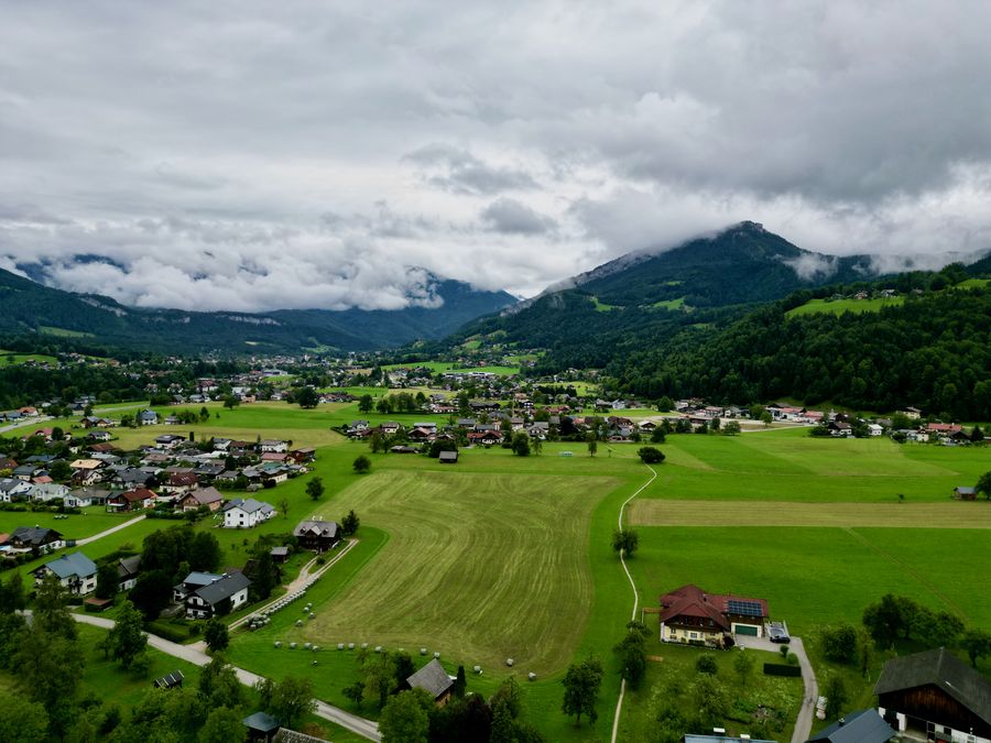 A green valley with a village and fields under low clouds, seen from above