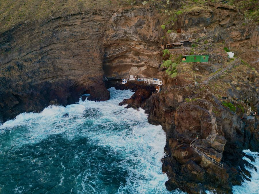 Waves breaking against dark volcanic sea cliffs, seen from above