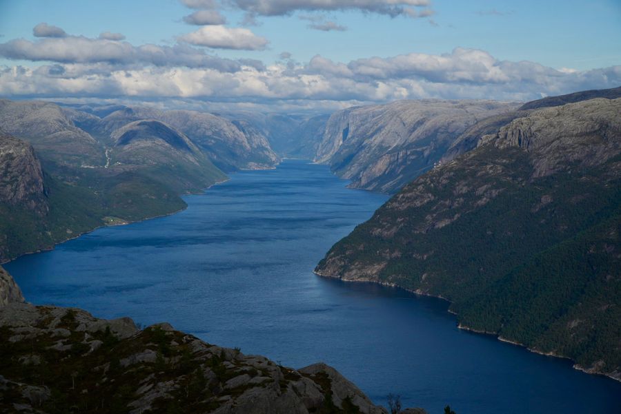 A long fjord between steep green mountains under scattered clouds
