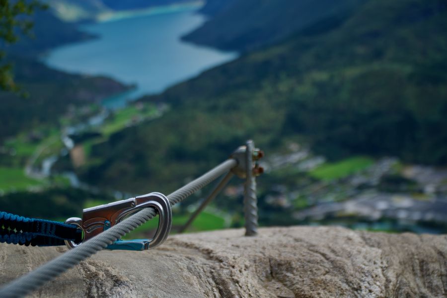 A steel climbing cable anchored to rock, with a fjord far below