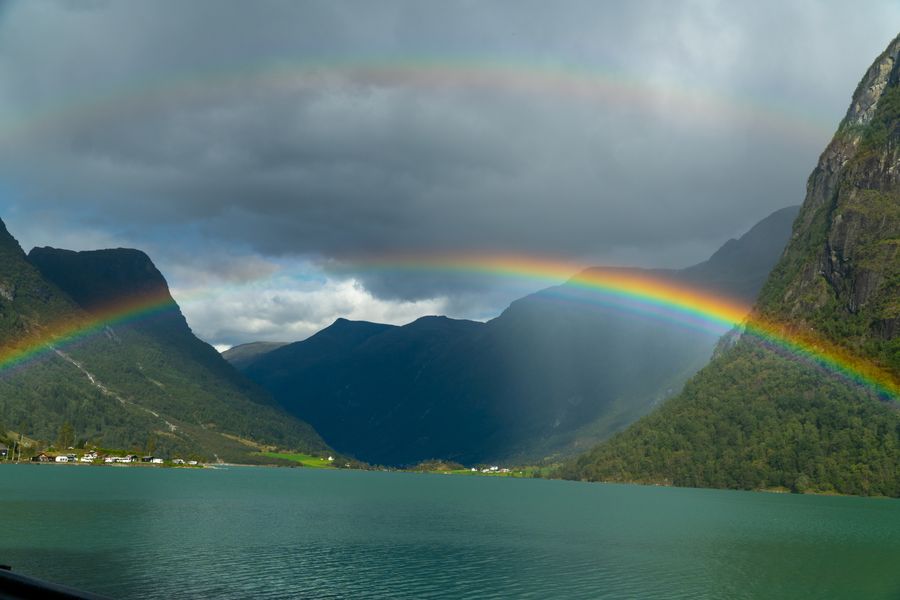 A rainbow arching over a fjord between steep mountains