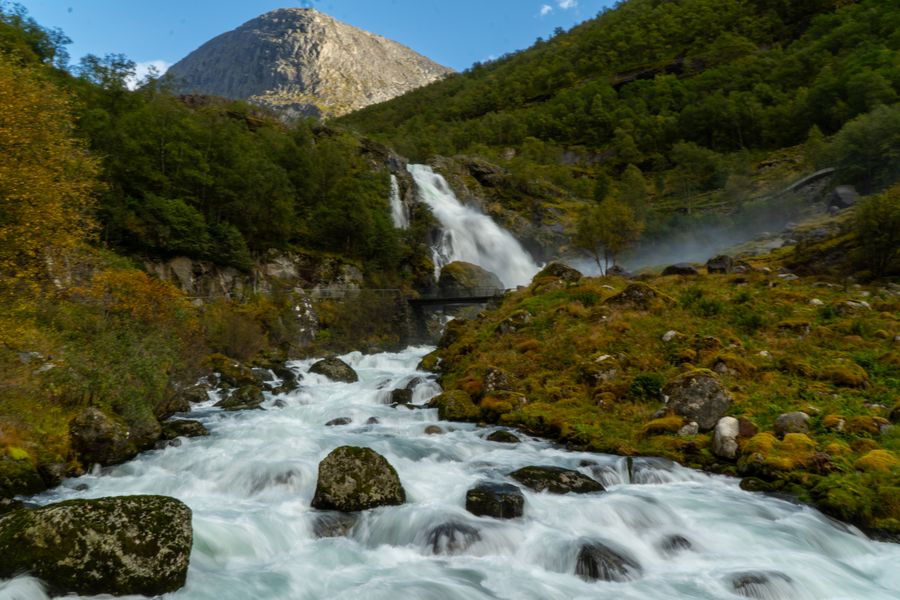 A waterfall feeding a rushing stream below a mountain