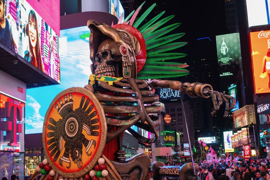 A giant skeleton figure with a feathered headdress among bright billboards