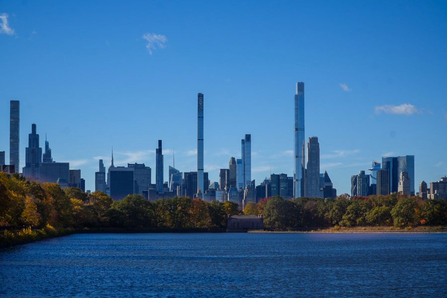 A skyline of slim towers above a lake and autumn trees