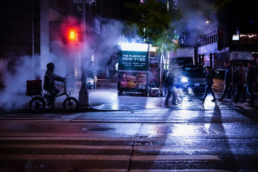 Steam and a red light over a wet night street as a cyclist crosses
