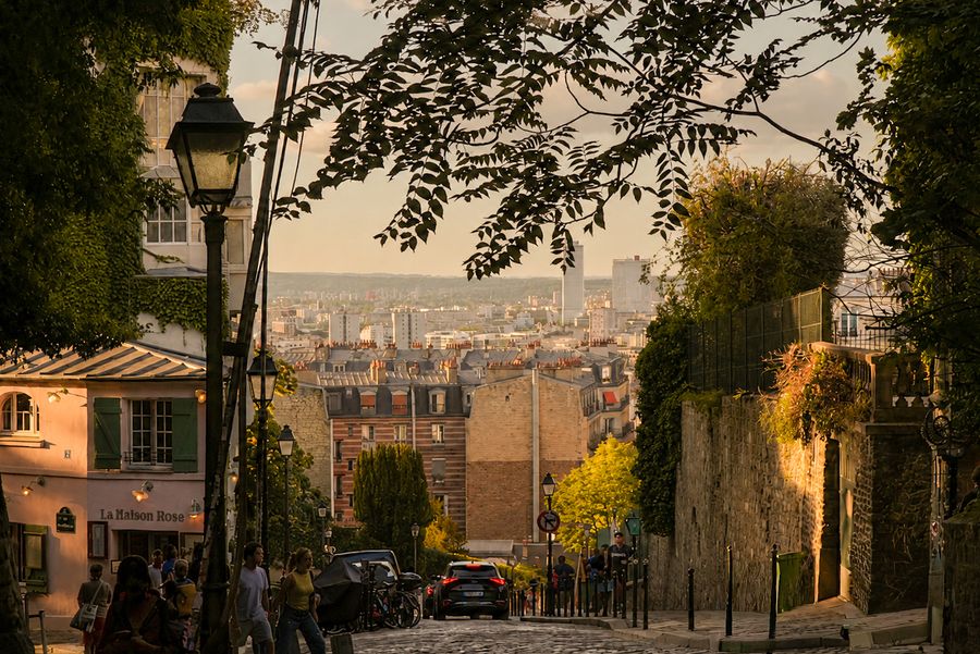 A cobbled hill street with a lamp post and the city glowing below