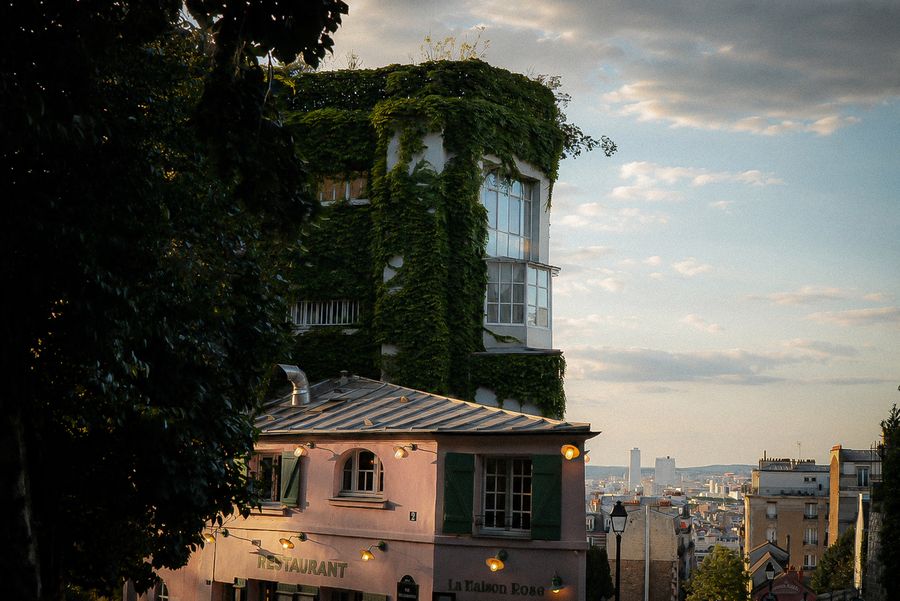 An ivy-covered house above a sloping street, the city in the distance