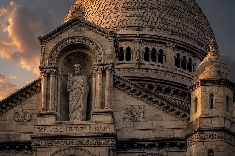 A carved stone statue in an arch below a large dome at sunset