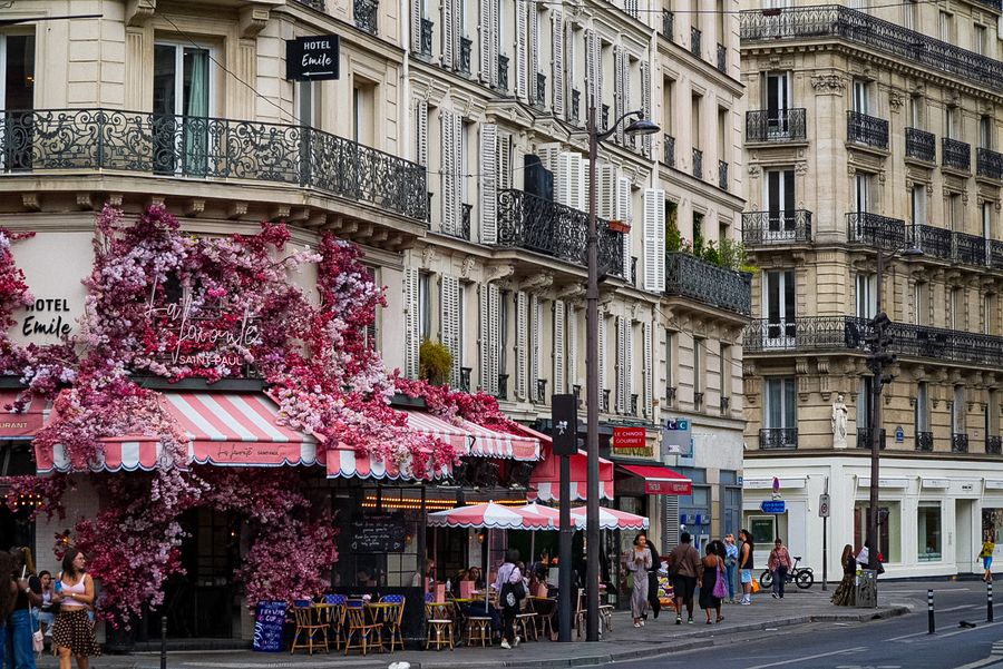 A Paris café covered in pink flowers on a busy corner