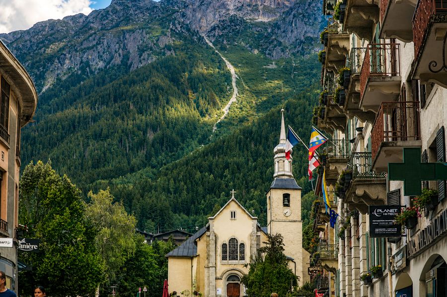 A white church spire in a mountain village beneath forested slopes