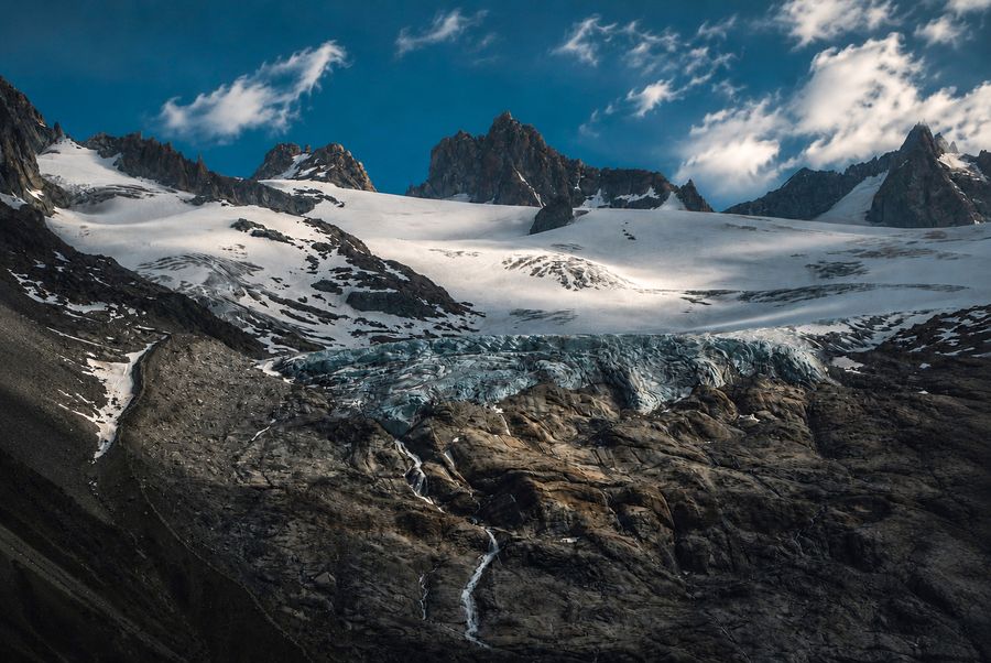 A broad glacier beneath rocky peaks and bright clouds