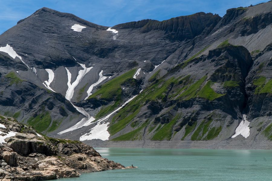A milky turquoise reservoir below snow-streaked grey mountains
