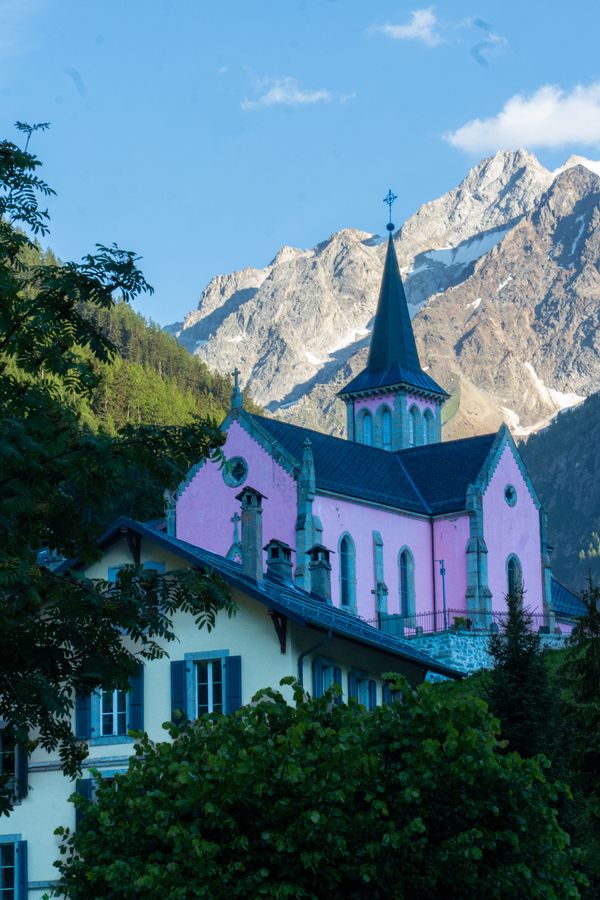 A pink chapel in front of jagged snowy peaks