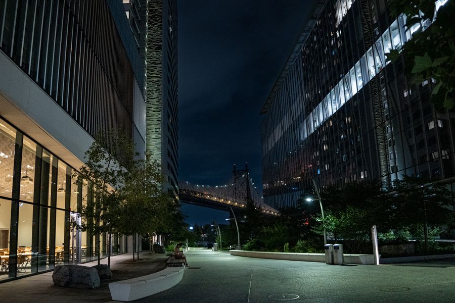 A quiet modern street at night with a lit bridge in the distance