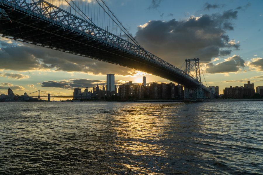 A suspension bridge silhouetted against a sunset over the river