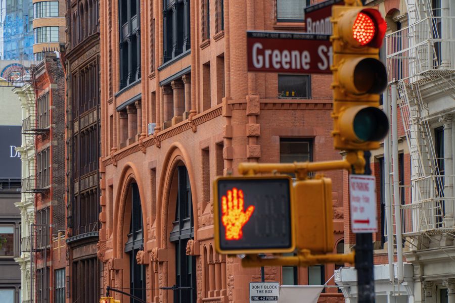 A red traffic hand and a Greene Street sign against red brick buildings