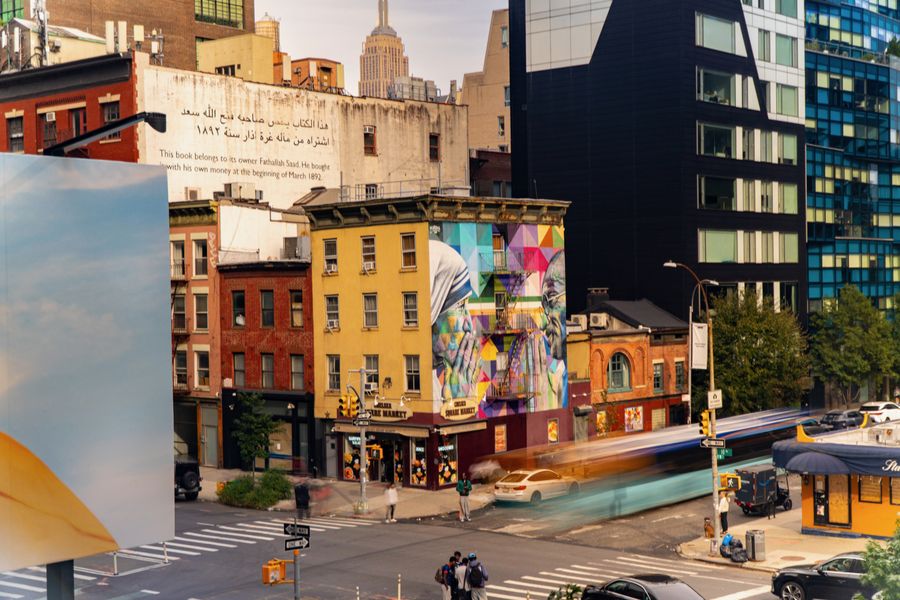 Colourful low buildings and a mural at a busy corner, with tall towers behind